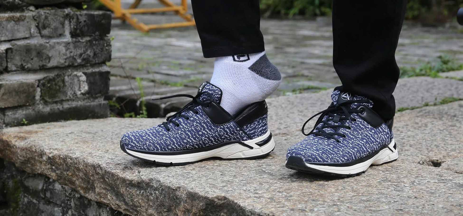 A pair of navy knit Zeba sneakers worn with white socks on a stone step outdoors